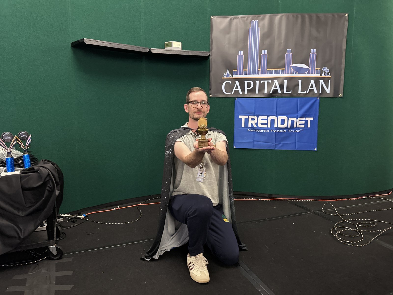 Attendee kneeling with trophy in front of Capital LAN banner