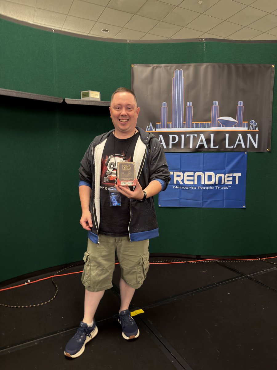 Attendee holding a boxed game in front of Capital LAN banner