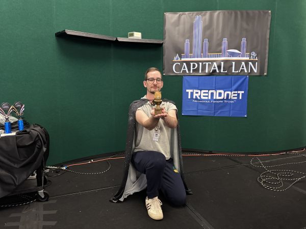 Attendee kneeling with trophy in front of Capital LAN banner