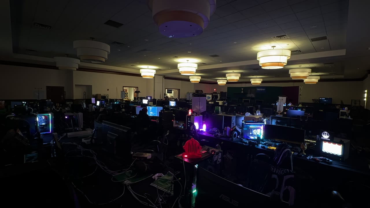 Dimly lit BYOC hall with illuminated gaming setups