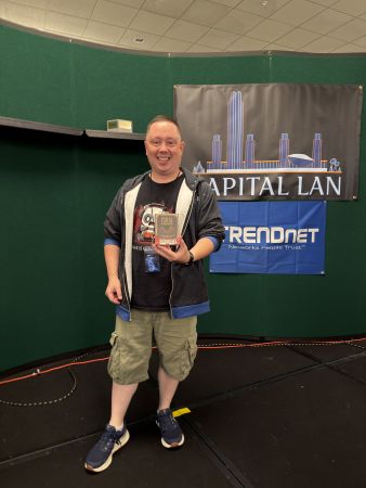 Attendee holding a boxed game in front of Capital LAN banner