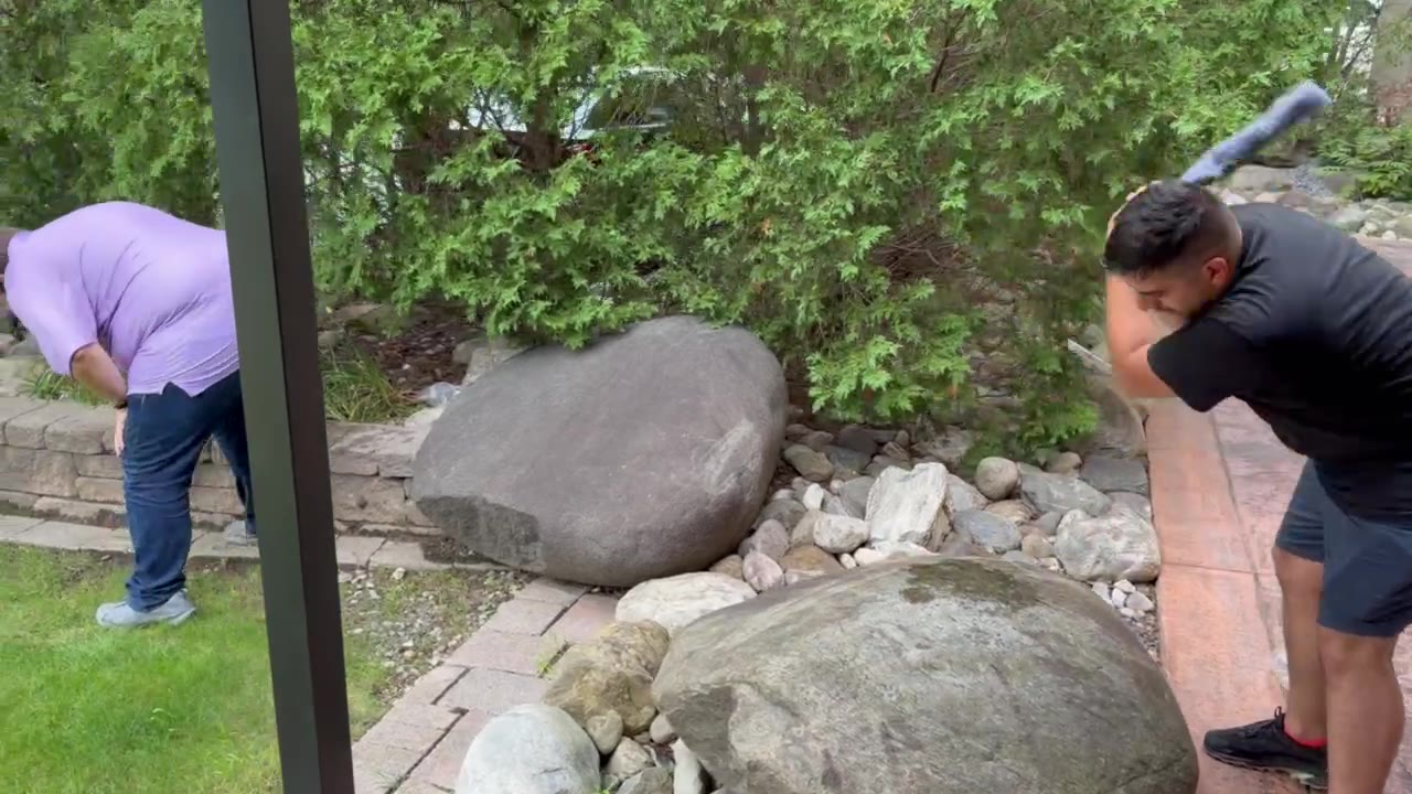 Two people smashing rocks with tools outdoors